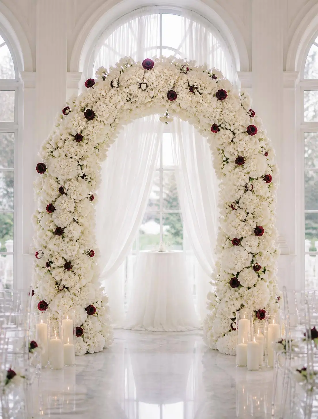 White floral ceremony arch with deep crimson rose accents and pillar candles