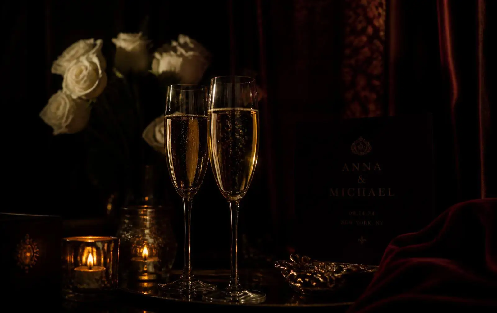 Champagne flutes glowing in candlelight against deep crimson velvet